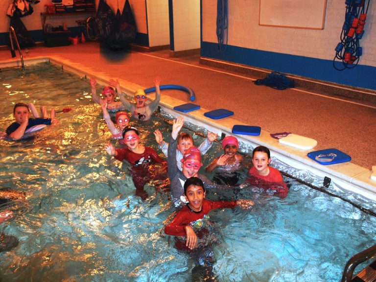 Happy kids in the pool during swimming lesson